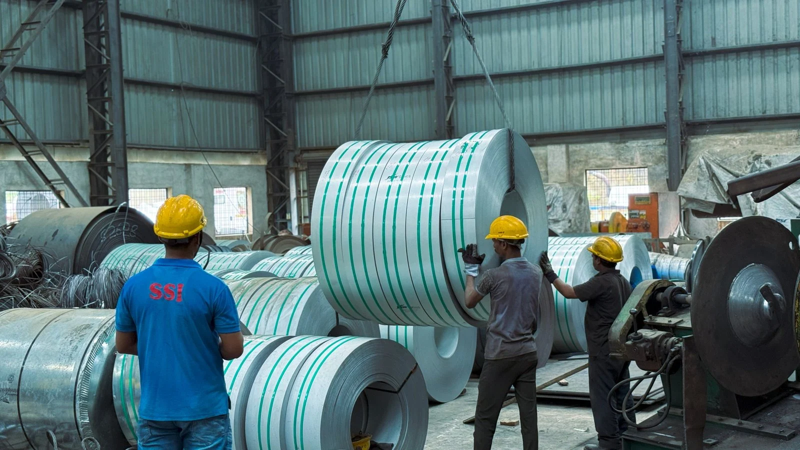 Factory workers handling a wrapped steel coil