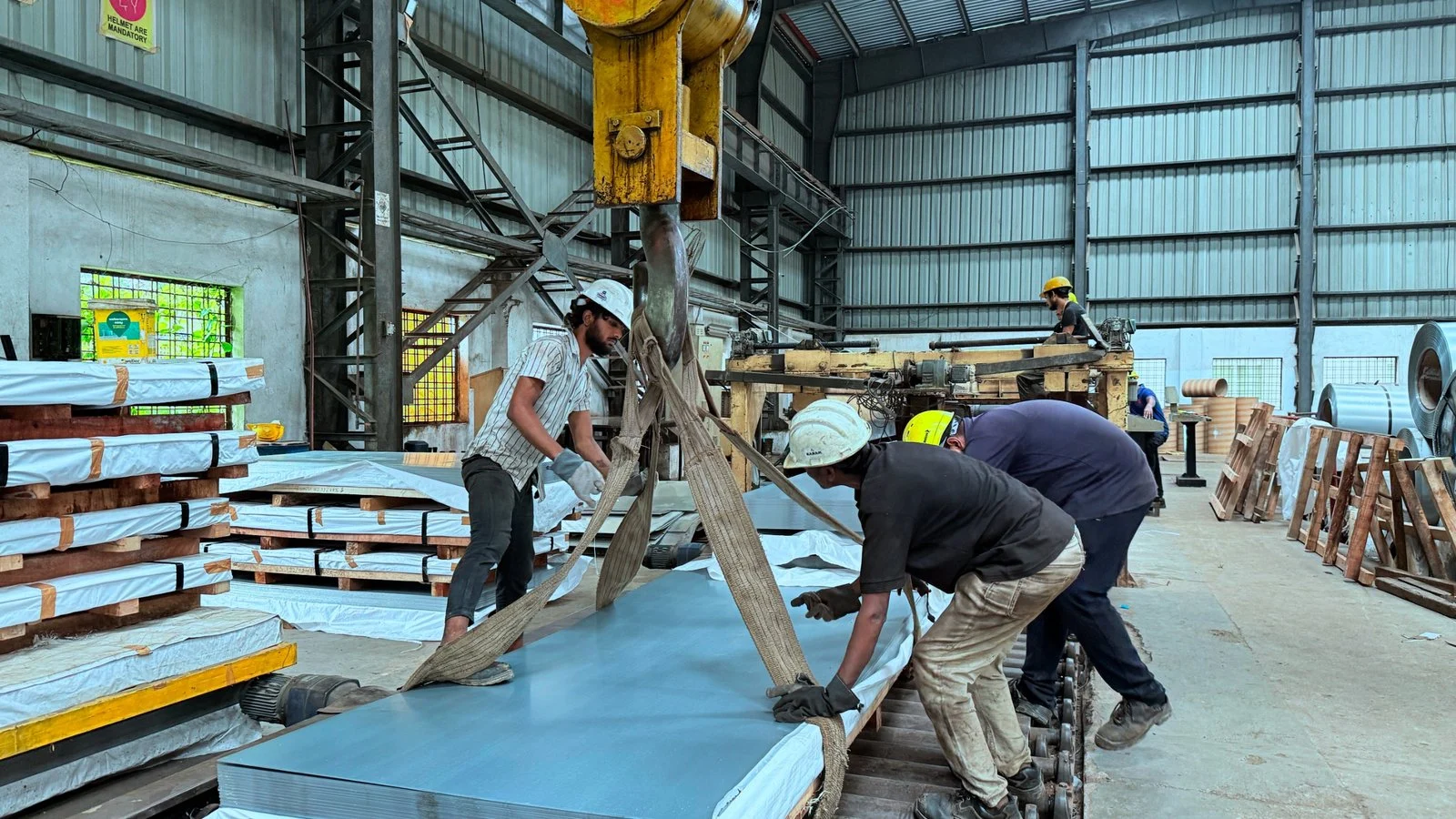 Workers preparing steel sheets for lifting with a crane